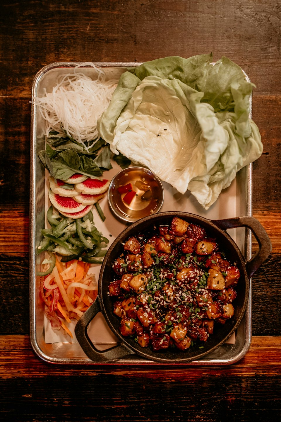 Meal with glazed meat, noodles, and vegetables on a metal tray.