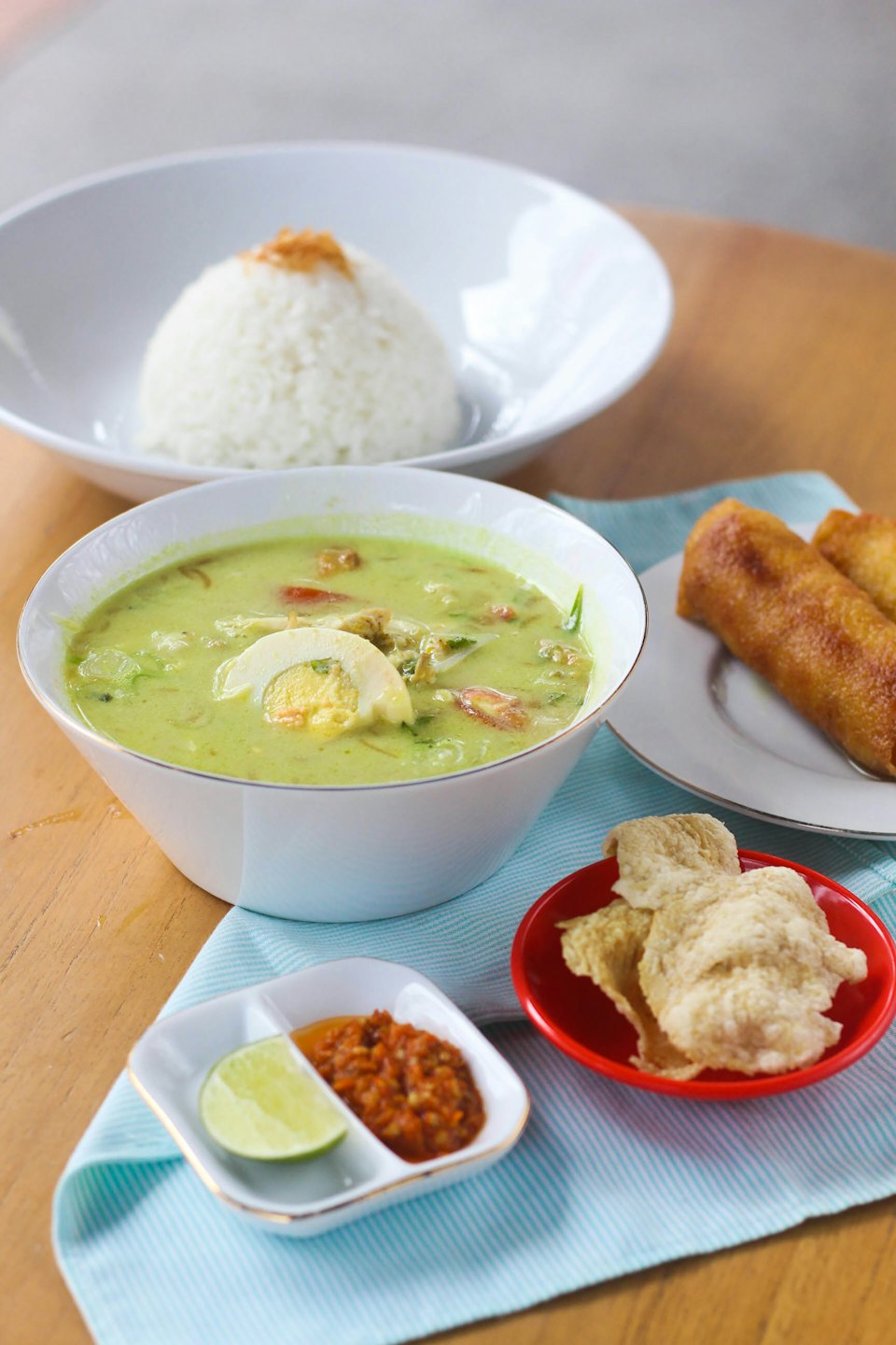 Indonesian meal with soup, rice, spring rolls, and crackers.
